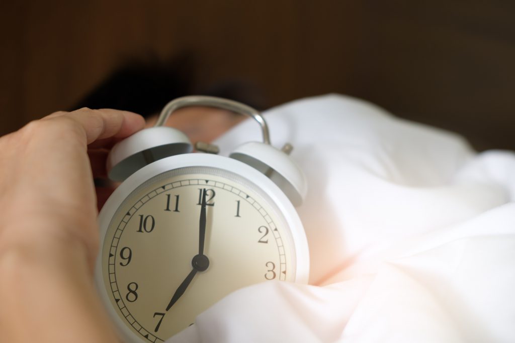 man holds clock in bed to get more sleep